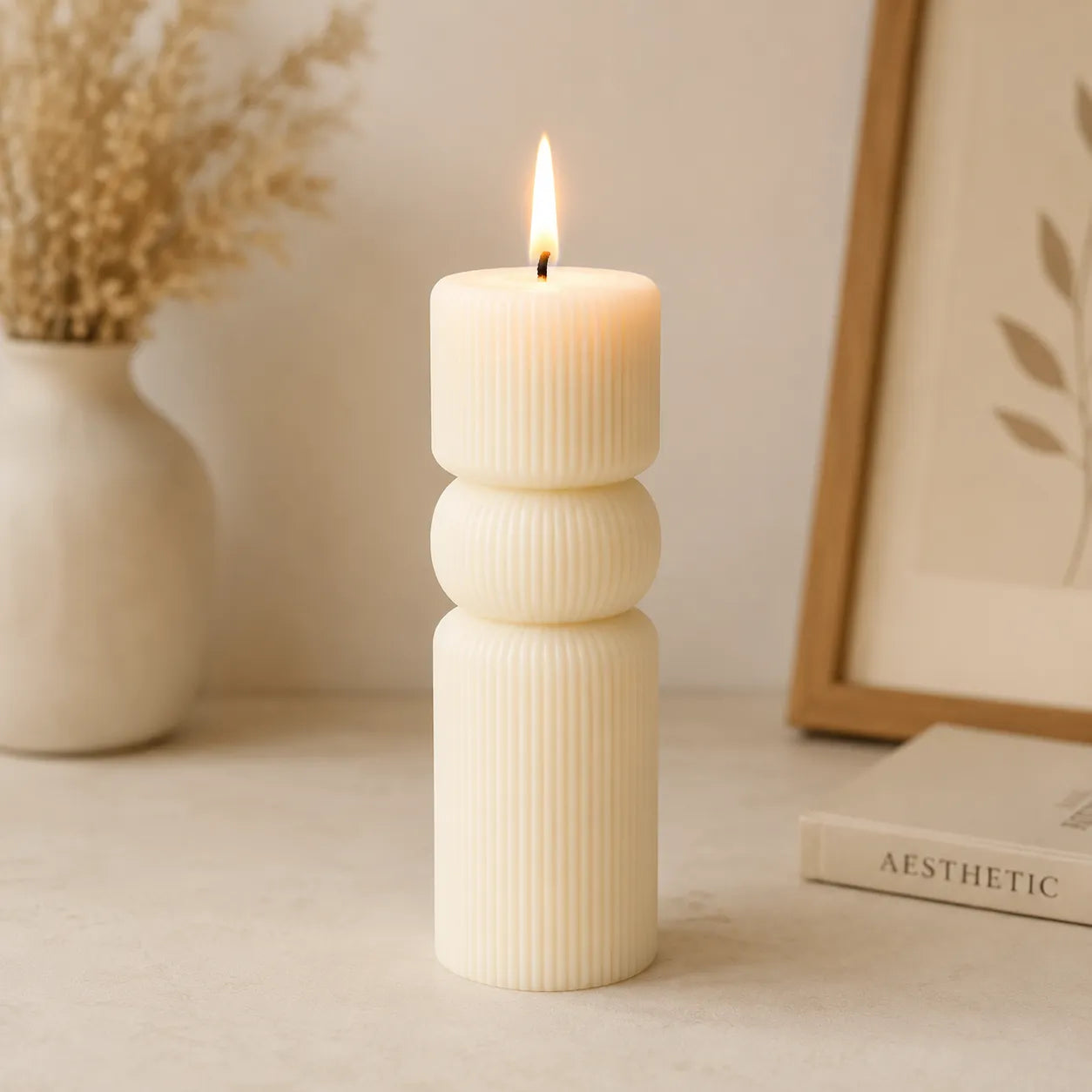 Decorative candle with ribbed texture on a surface with a vase and framed picture in the background.