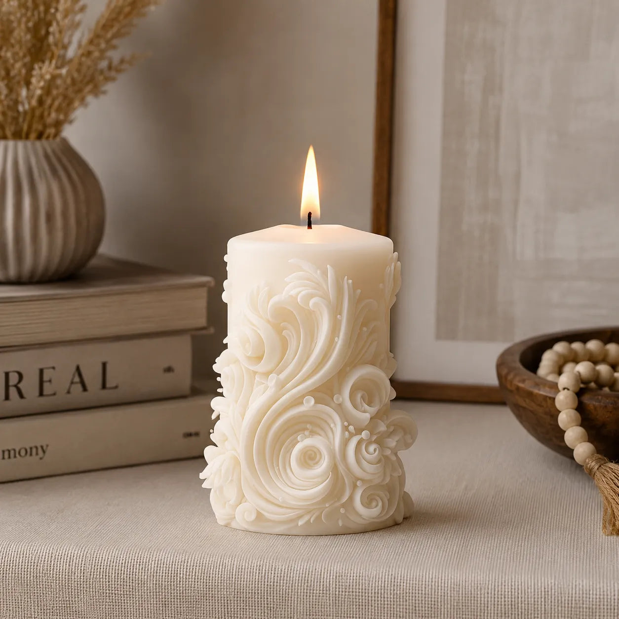 Decorative candle with intricate patterns on a surface with books and a vase in the background.